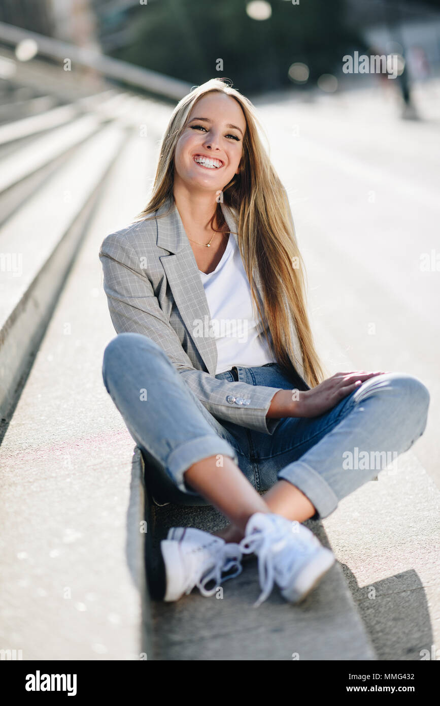 Bellissima giovane donna caucasica sorridente in background urbano. Ragazza bionda indossando abiti casual in strada. Femmina con elegante e camicia blu jean Foto Stock