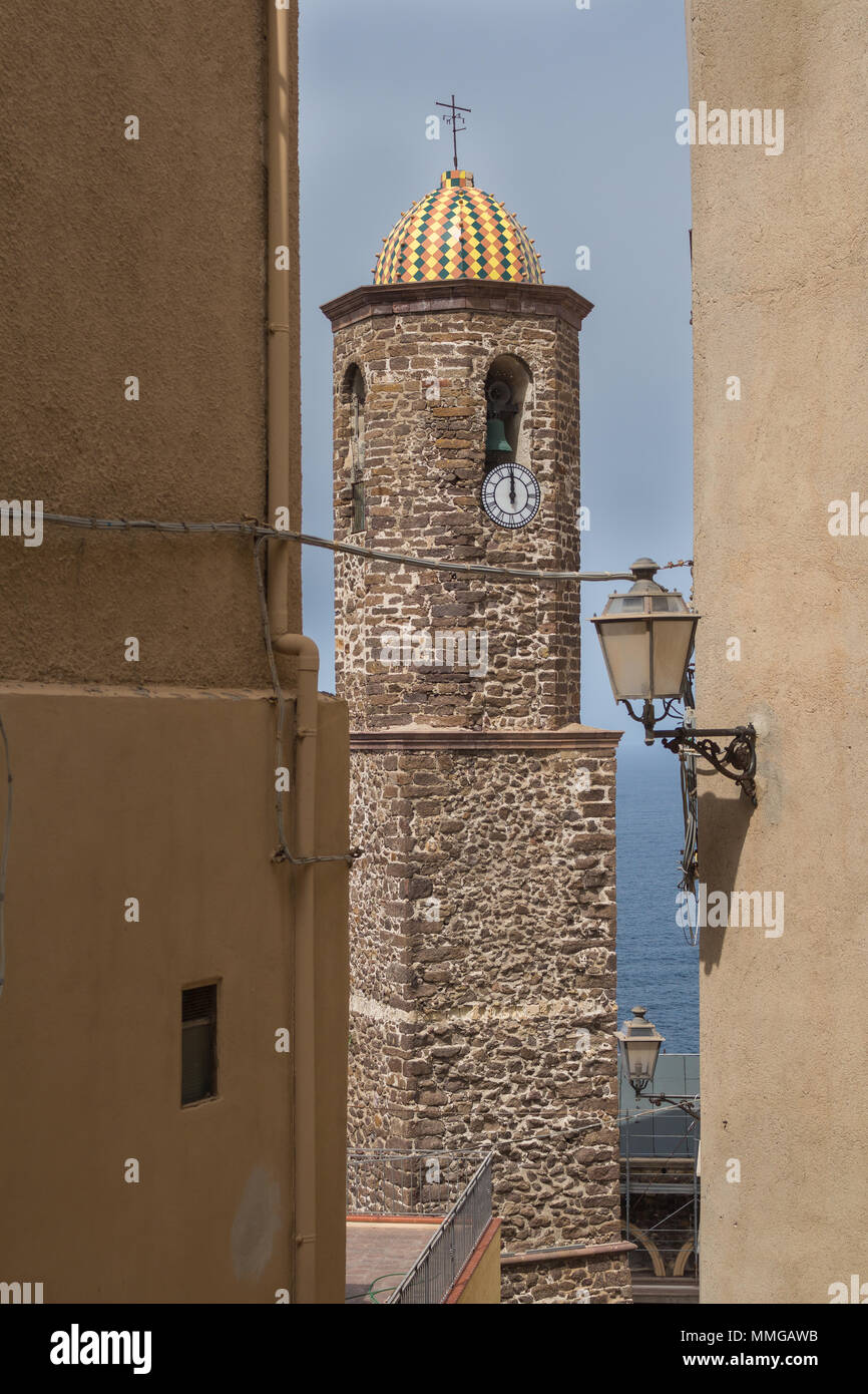 Cupola colorata in corrispondenza di una torre di Sant Antonio chiesa in Castelsardo, Sardegna, Italia. Vecchia Lanterna sul muro di una casa in primo piano, mare un cielo in Foto Stock