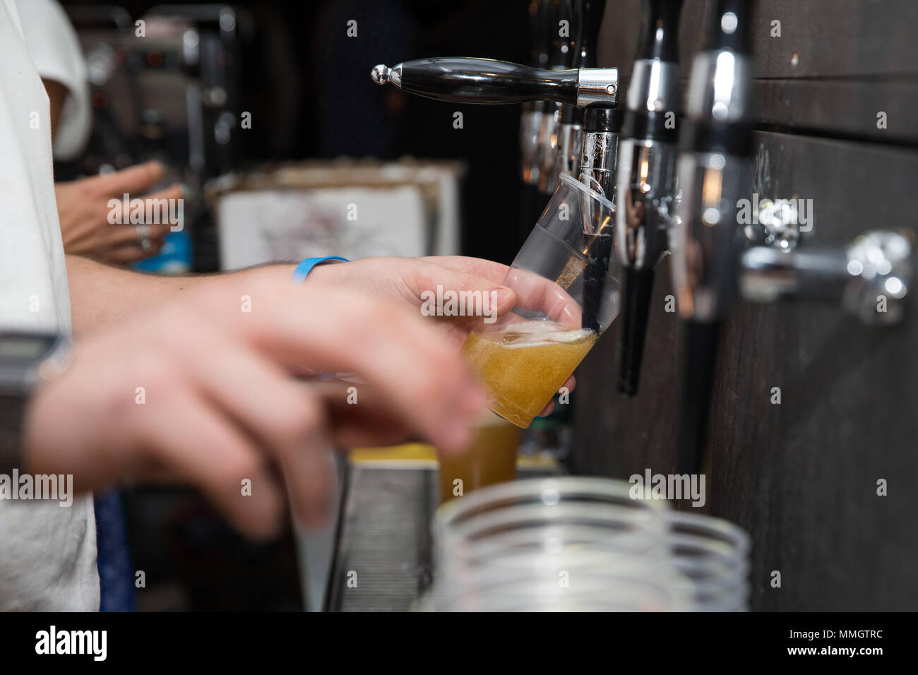 Primo piano di un barman versando una birra bionda in tap in un bicchiere di plastica con soggetti e concentrarsi sulla destra Foto Stock