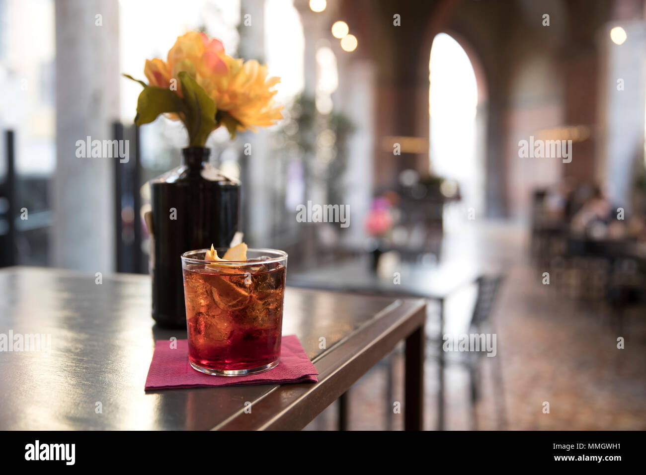Primo piano di un tavolo bar, un bicchiere di cocktail americano pronto a bere con un fiore accanto ad essa, soggetto e concentrarsi sulla sinistra Foto Stock