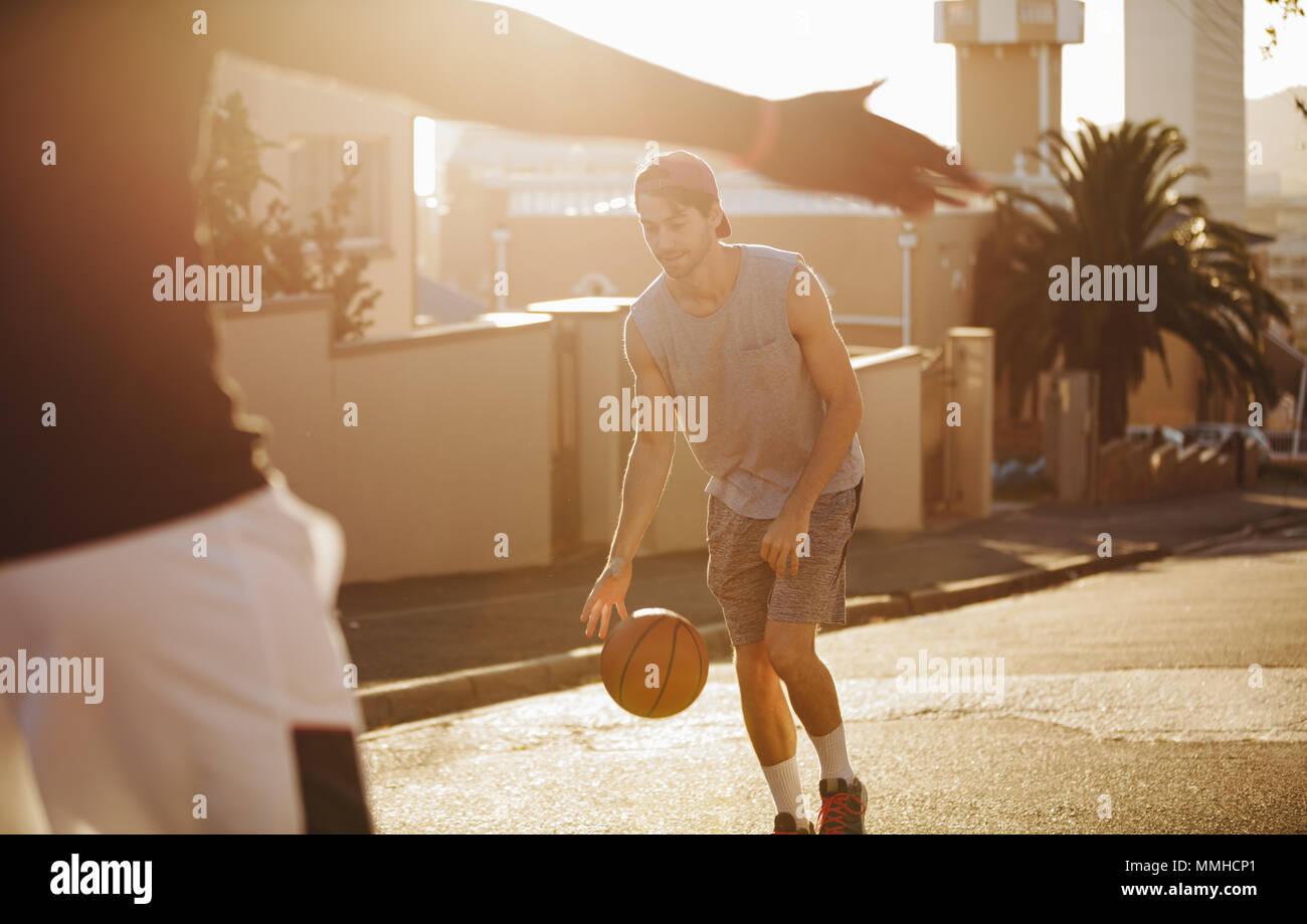 Giovane uomo gioca con la pallacanestro su strada. L'uomo la pratica di gioco del basket in una giornata di sole su una strada vuota. Foto Stock
