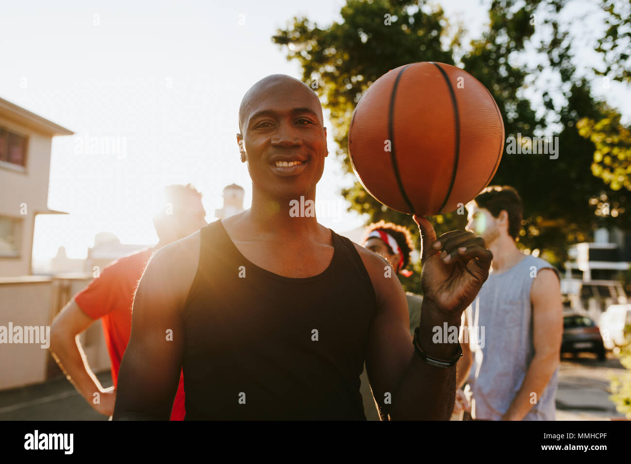 Quattro uomini di basket a piedi giù per la strada dopo una partita di basket. Uomo di pallacanestro di filatura sul suo pollice. Foto Stock