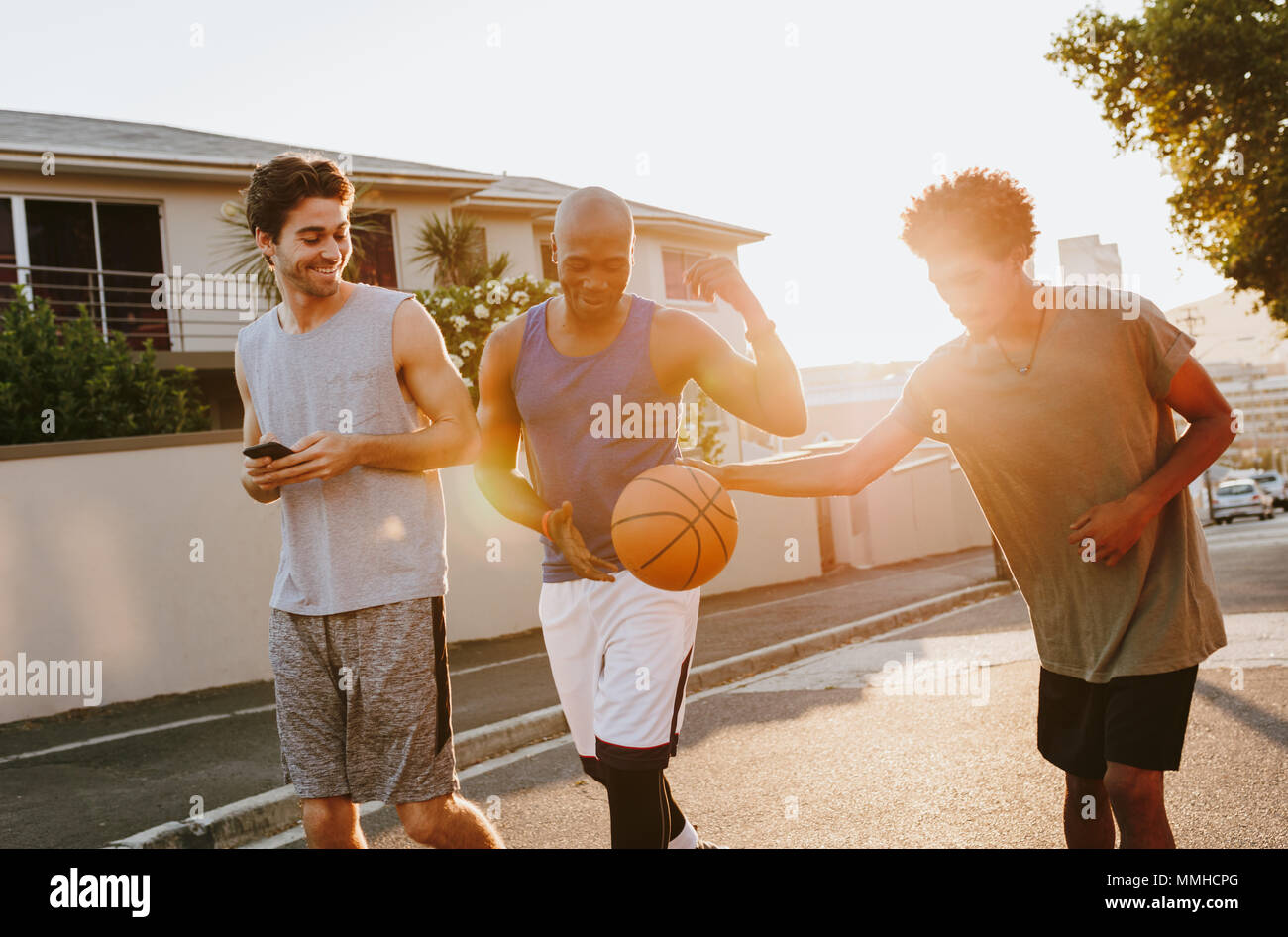 Tre uomini di basket a piedi giù per la strada a suonare con la palla. Gli uomini camminare indietro dopo una partita di basket. Foto Stock