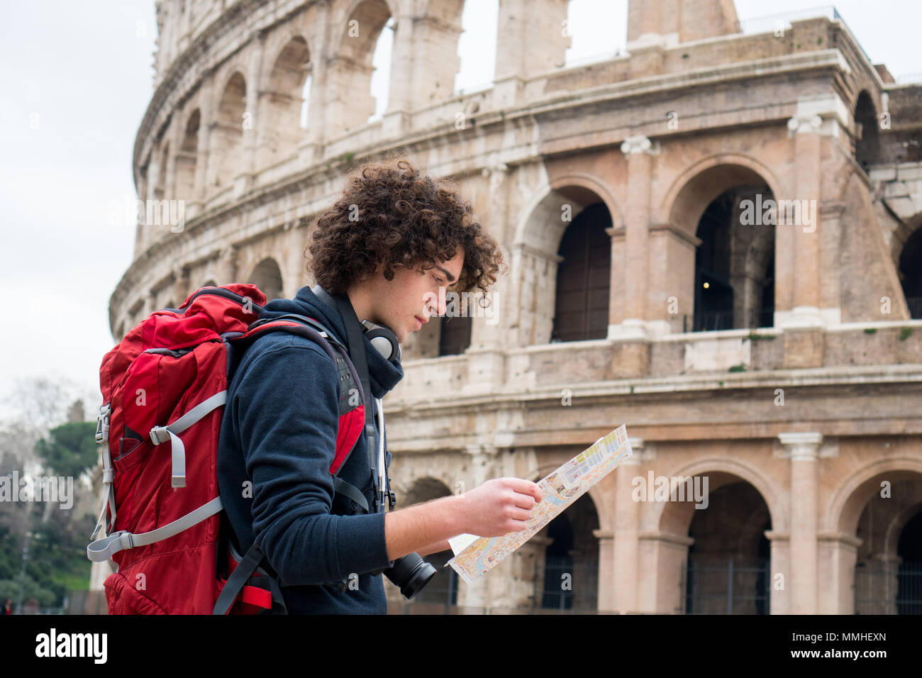 Bel giovane viaggiatore guardando la mappa turistica di Roma davanti al Colosseo. Zaino in spalla con la fotocamera e la mappa turistica Foto Stock