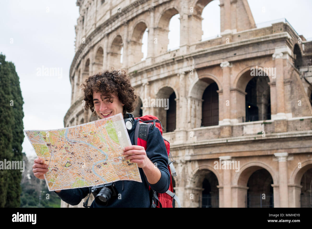 Bel giovane viaggiatore guardando la mappa turistica di Roma davanti al Colosseo. Zaino in spalla con la fotocamera e la mappa turistica Foto Stock