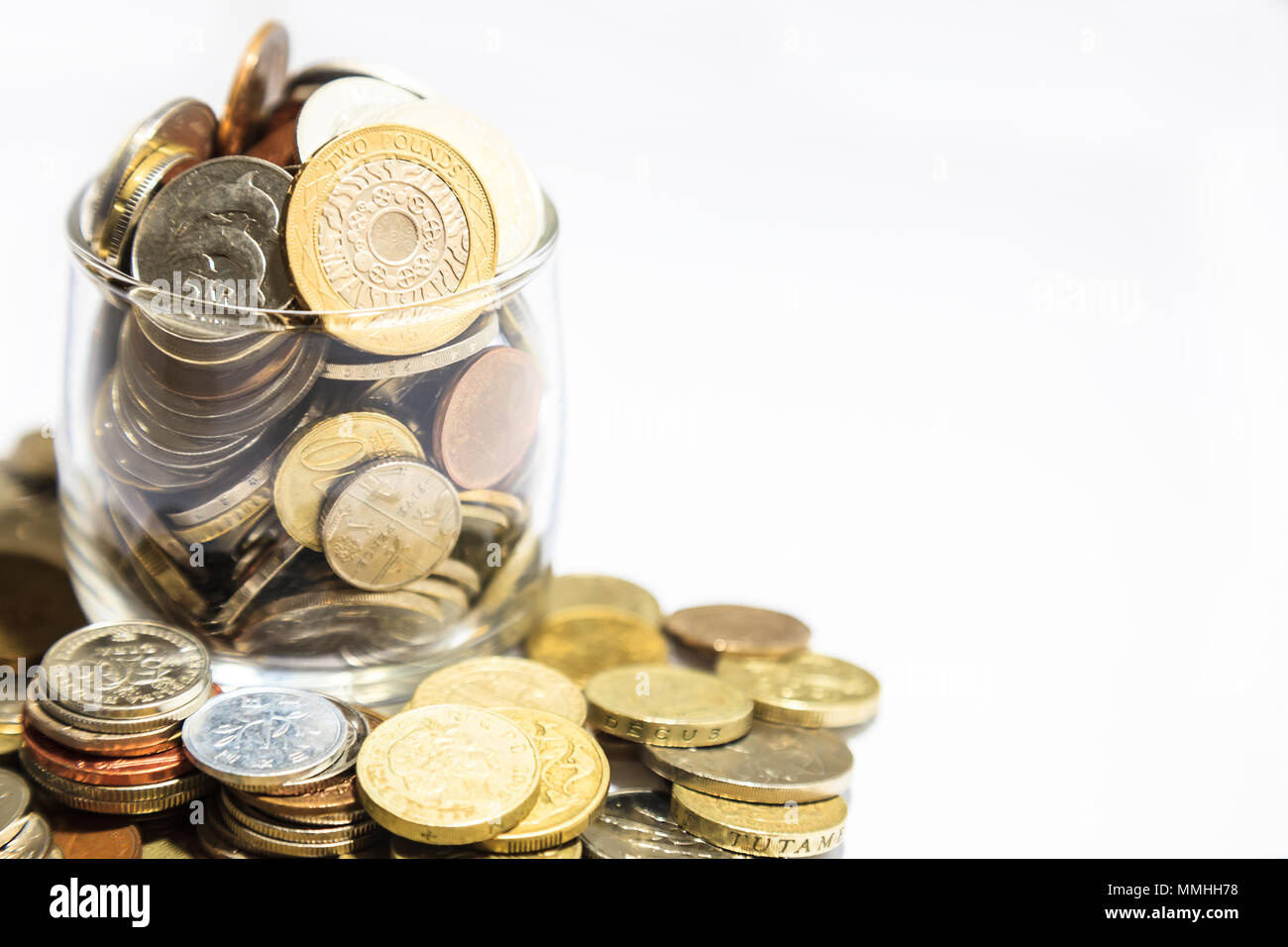 Vasetto di denaro, varie monete in valuta traboccante su sfondo bianco Foto Stock
