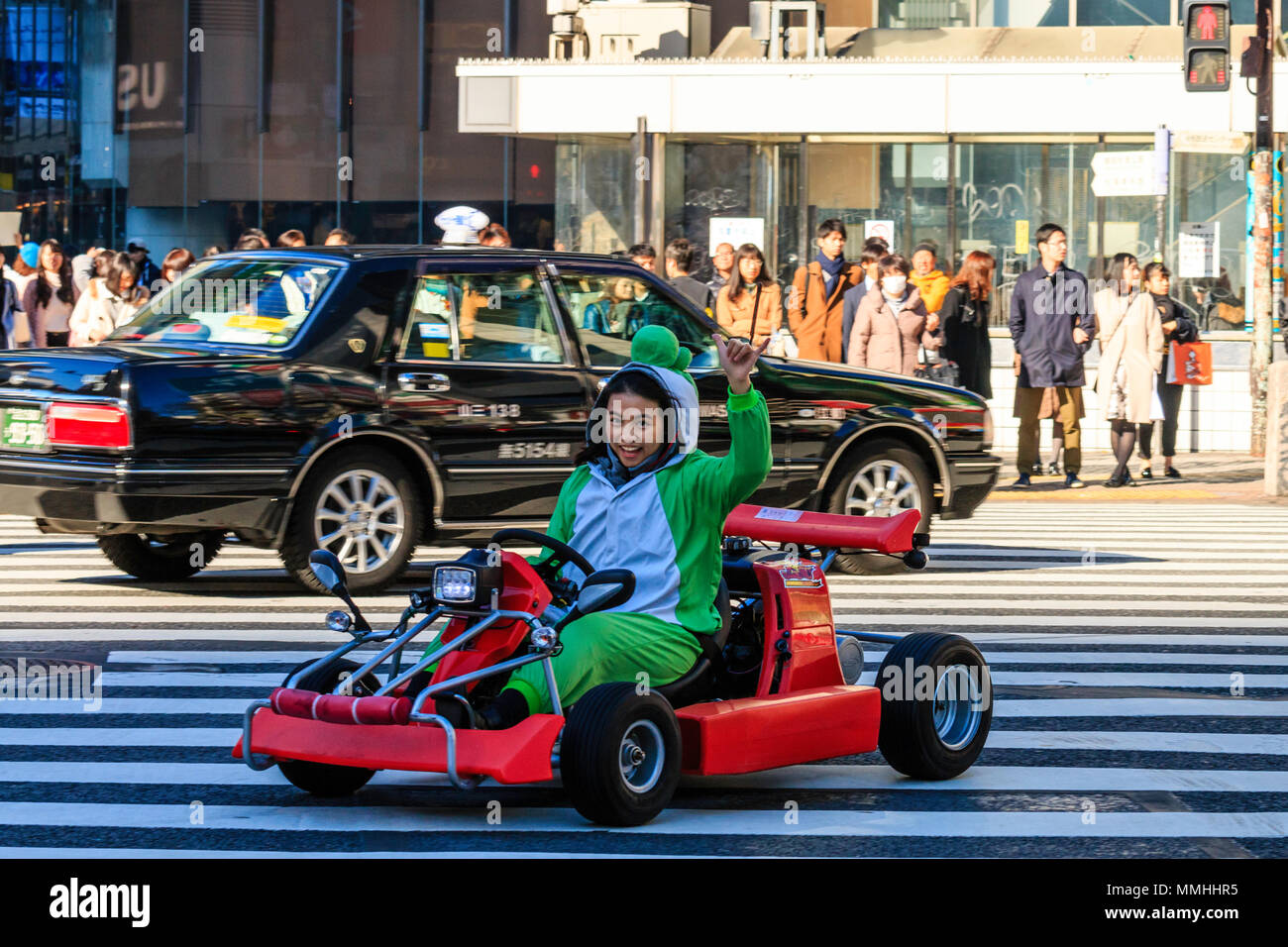 Tokyo, Shibuya crossing. Popolari attività turistiche, guida MariCar, Mario Kart mentre vestita come Mario carattere. Donna sventolare, guida, contatto visivo Foto Stock