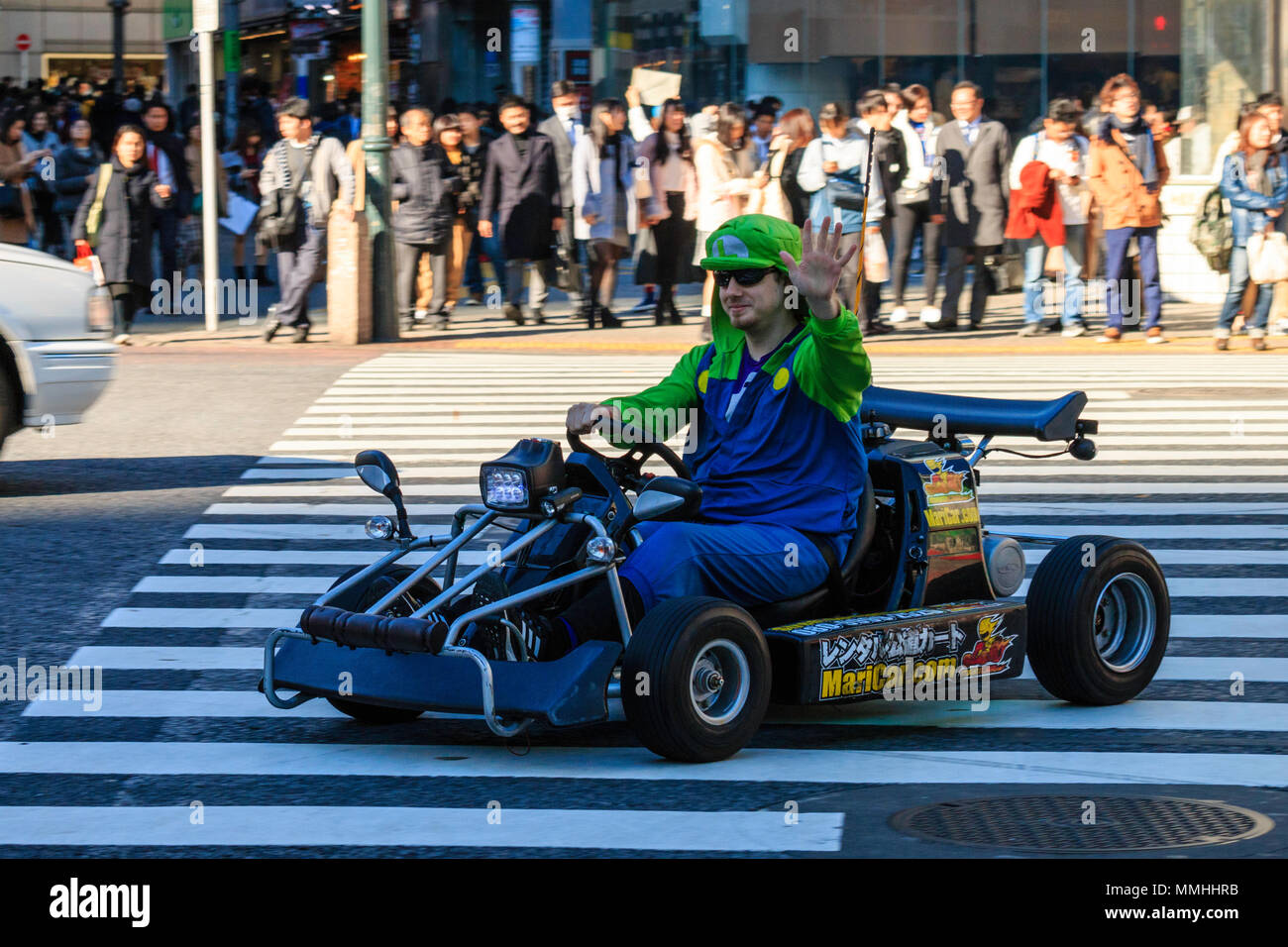 Tokyo, Shibuya crossing. Popolari attività turistiche, guida MariCar, Mario Kart mentre vestita come Mario carattere. L'uomo sventolando durante la guida. Foto Stock
