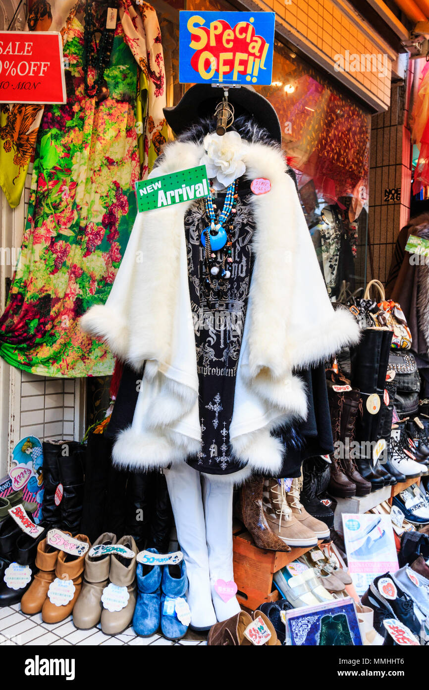 Tokyo, Harajuku, Takeshita street. Donna bianco mantello di pelliccia, gotico nero t-shirt e gambali in bianco su supporto, segno 'nuovo arrivo' e 'speciale offerta'. Foto Stock