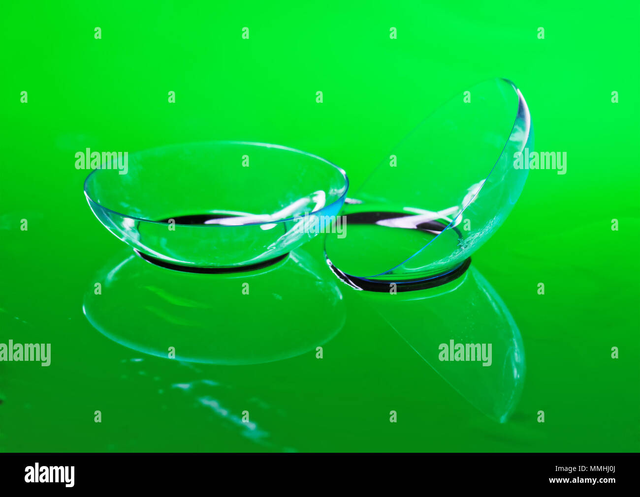 Trasparente lenti a contatto per la correzione di visione giacciono su uno specchio superficie bagnata. Sfondo verde Foto Stock