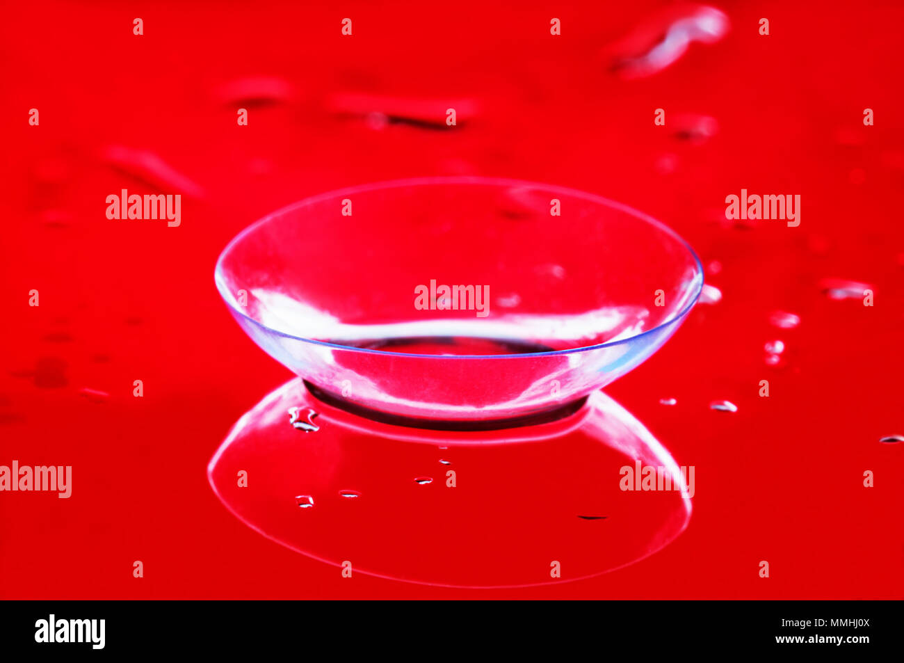 Uno trasparente lente a contatto per la correzione vista da vicino. Specchio superficie bagnata, comune sfondo rosso Foto Stock