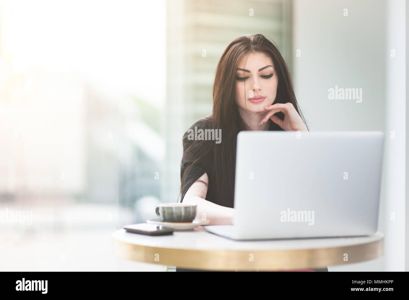 Bella ragazza caucasica seduta a tavola con la tazza di caffè in linea di lavoro sul computer portatile Foto Stock