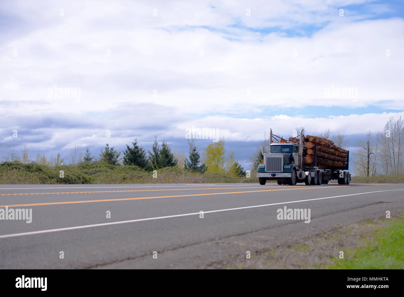 Blu scuro classic potente big rig semi carrello il trasporto commerciale di legname di legno sul letto piano semi rimorchio nell'appartamento strada diritta in American Nort Foto Stock