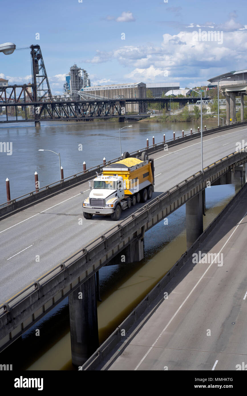 Big Rig potente classico giallo ribaltabile semi autocarro con cassone coperto porta commerciale cargo in esecuzione sul cavalcavia intersezione strada lungo il fiume e Foto Stock