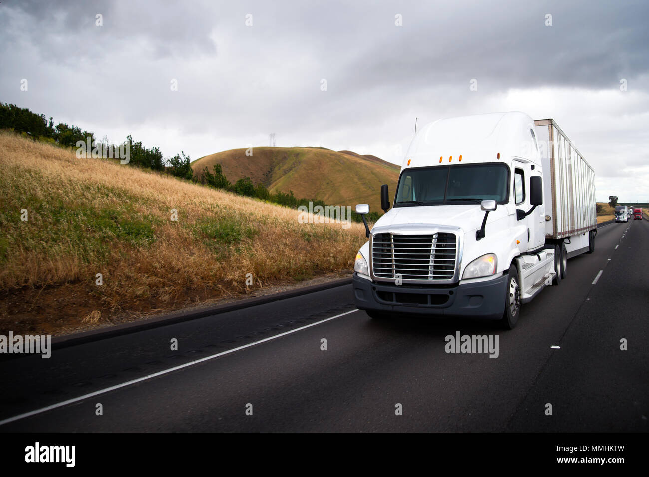 White big rig semi carrello con dry van semi rimorchio la guida di fronte a un altro traffico di semi camion sul rettilineo interstate highway con giallo h Foto Stock