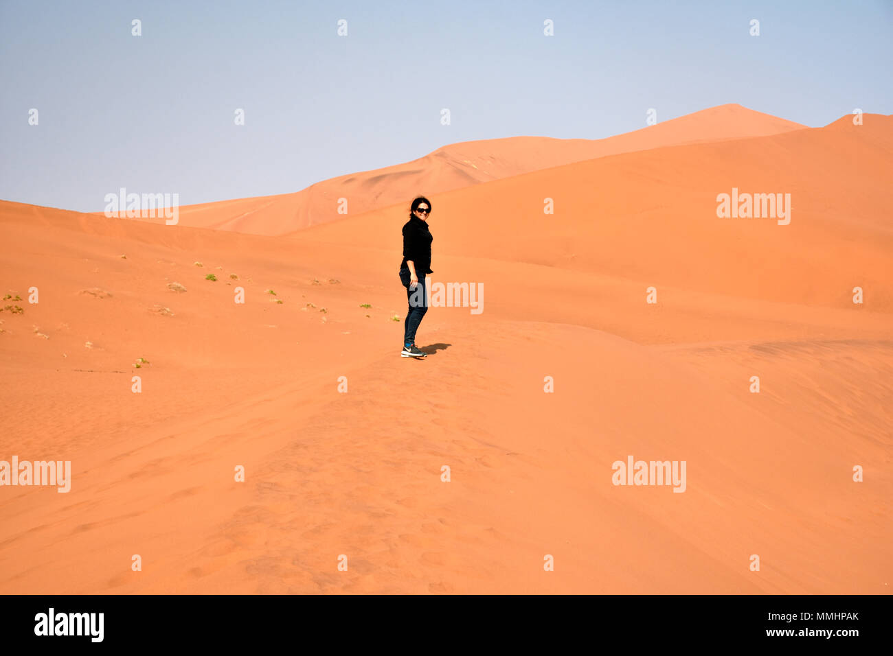 Donna cammina sulle dune rosse del Namib Desert, Namib Naukluft National Park, area Sossusvlei, Sesriem, Namibia Foto Stock