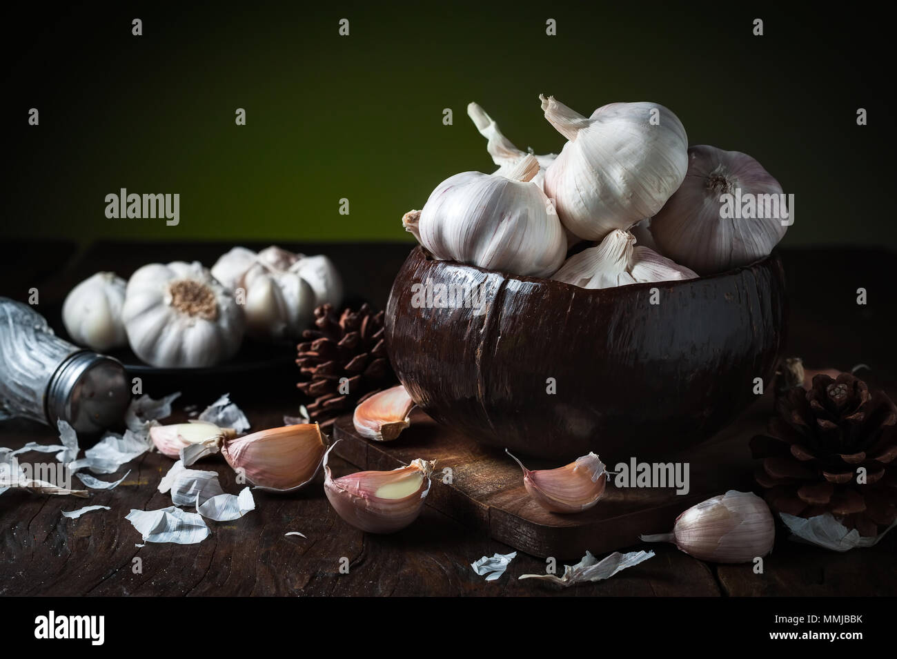 4 spicchi di aglio e aglio lampadina nella metà di guscio di noce di cocco ciotola sul tavolo di legno. Foto Stock