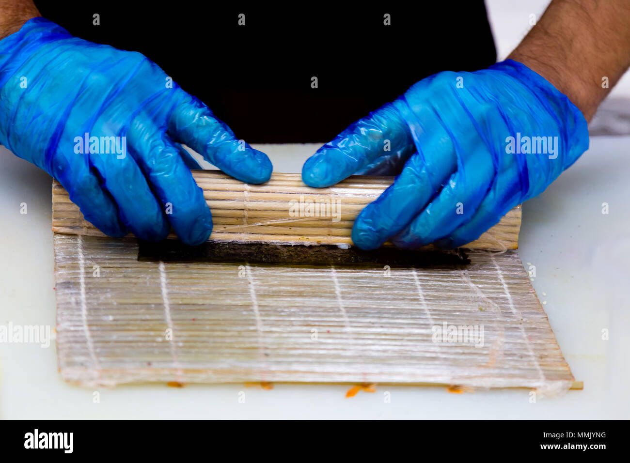 Preparazione di rotoli in un sushi bar. Un cuoco professionista indossando guanti blu è la preparazione tradizionale giapponese del cibo. Riso, cavolo riccio di mare, il cetriolo. Foto Stock