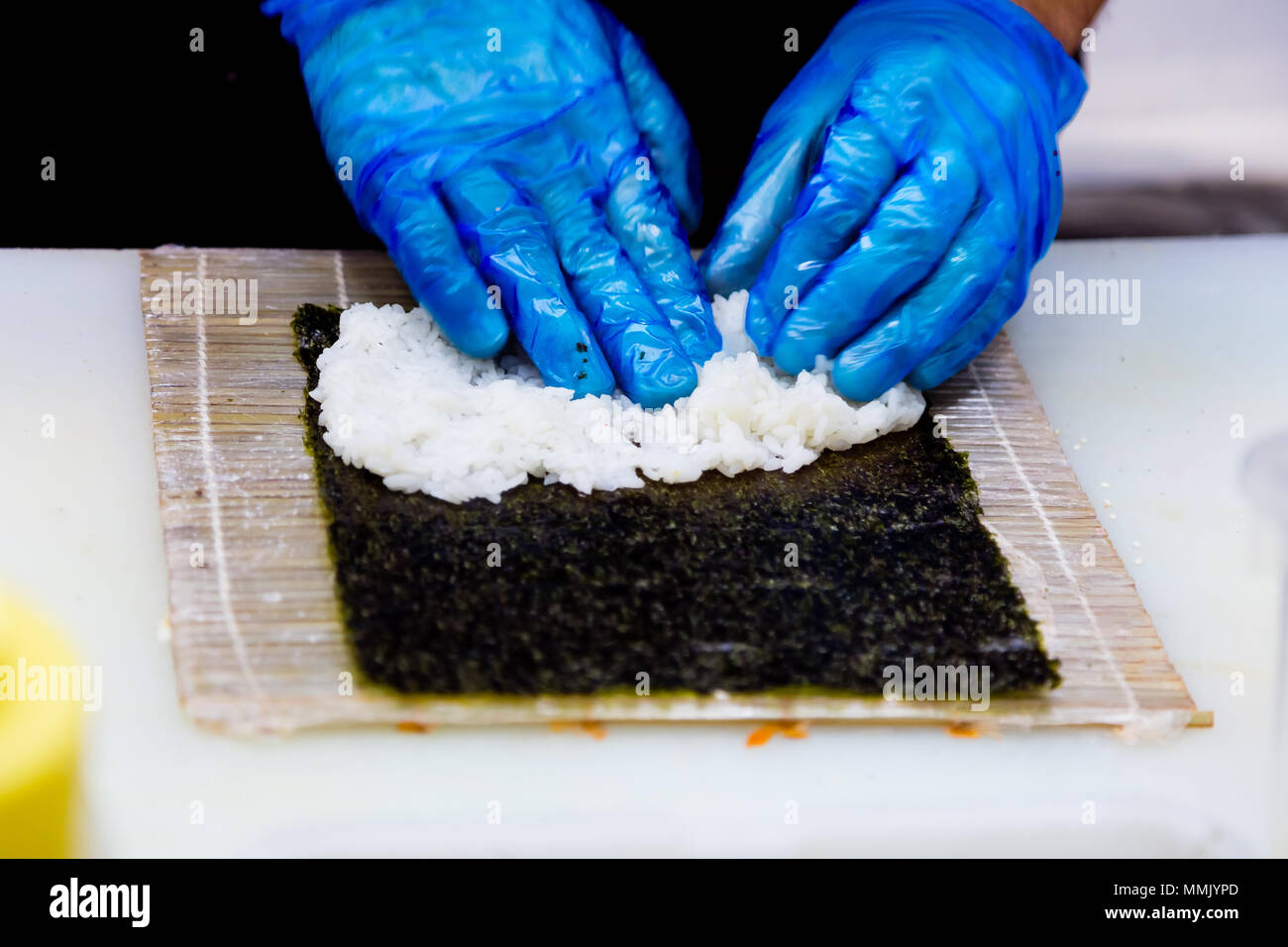Preparazione di rotoli in un sushi bar. Un cuoco professionista indossando guanti blu è la preparazione tradizionale giapponese del cibo. Riso, cavolo riccio di mare, il cetriolo. Foto Stock