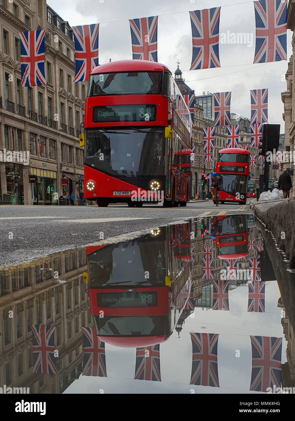 Londra. Regno Unito 12 maggio 2018 - La riflessione di Unione le bandiere e gli autobus in una pozza di acqua piovana. Bandiera dell'Unione pende al di sopra della Londra Regent Street davanti al Royal Wedding del principe Harry e Meghan Markle il 19 maggio in corrispondenza alla cappella di San Giorgio nel Castello di Windsor. Roamwithrakhee credito /Alamy Live News Foto Stock