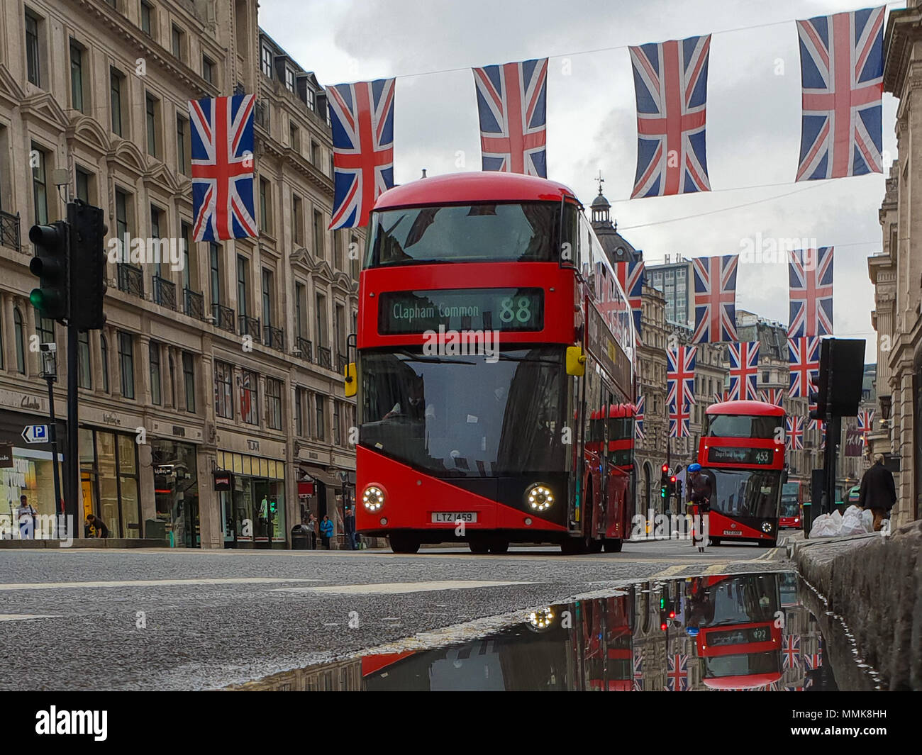 Londra. Regno Unito 12 maggio 2018 - La riflessione di Unione le bandiere e gli autobus in una pozza di acqua piovana. Bandiera dell'Unione pende al di sopra della Londra Regent Street davanti al Royal Wedding del principe Harry e Meghan Markle il 19 maggio in corrispondenza alla cappella di San Giorgio nel Castello di Windsor. Roamwithrakhee credito /Alamy Live News Foto Stock