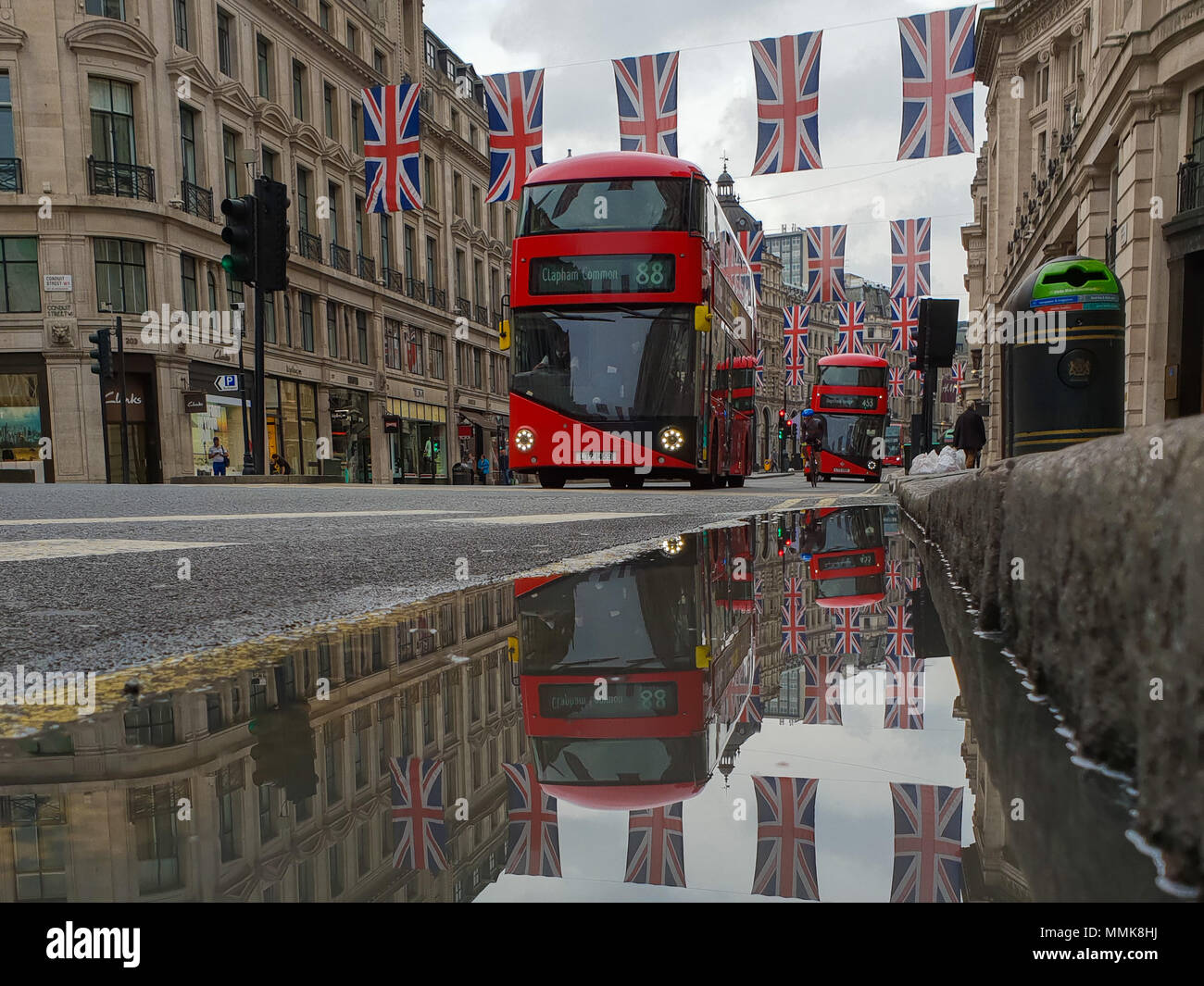 Londra. Regno Unito 12 maggio 2018 - La riflessione di Unione le bandiere e gli autobus in una pozza di acqua piovana. Bandiera dell'Unione pende al di sopra della Londra Regent Street davanti al Royal Wedding del principe Harry e Meghan Markle il 19 maggio in corrispondenza alla cappella di San Giorgio nel Castello di Windsor. Roamwithrakhee credito /Alamy Live News Foto Stock