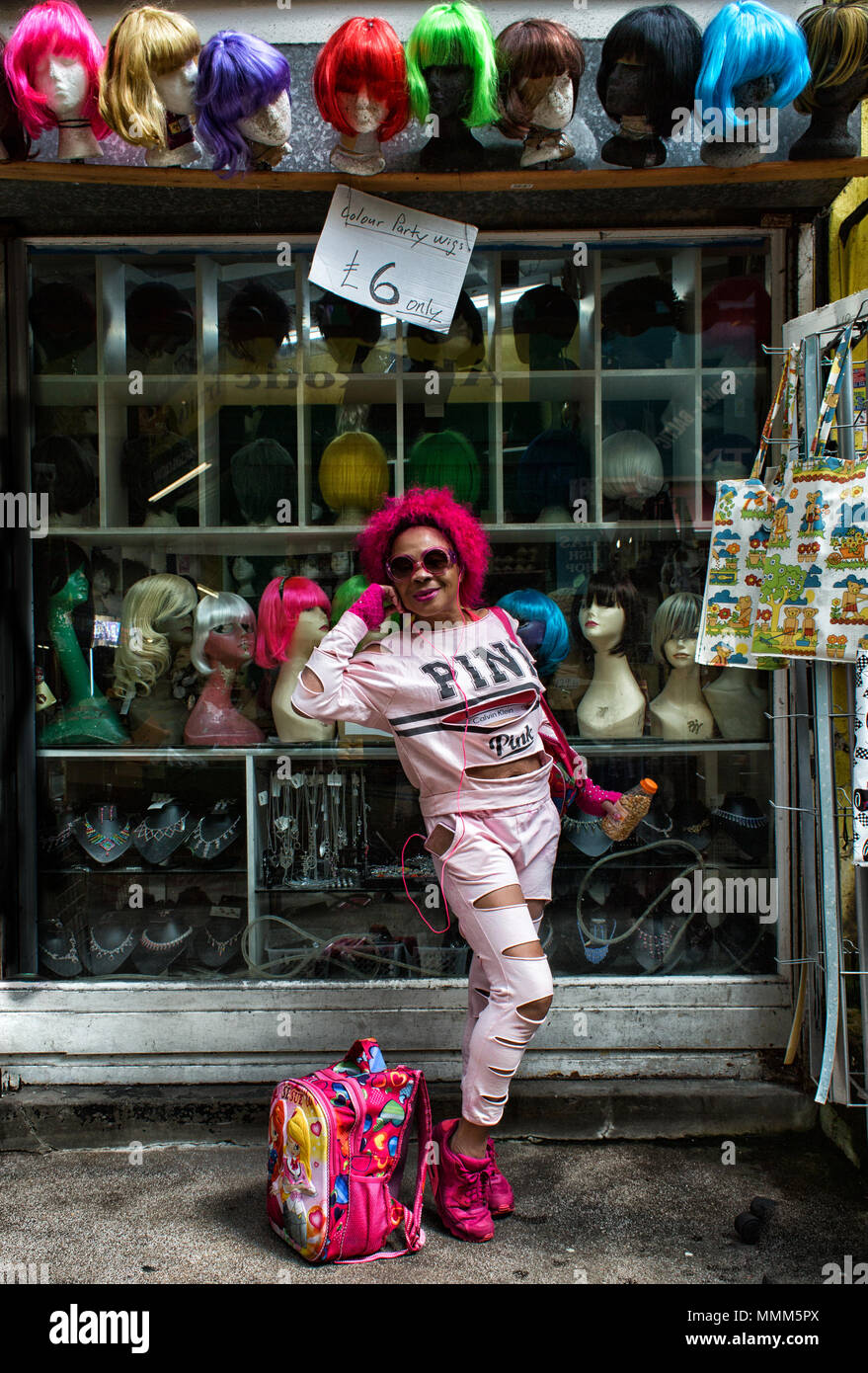 Signora vestita in rosa che indossa una parrucca rosa pone di fronte una parrucca shop in Brixton Village London SW2 Foto Stock