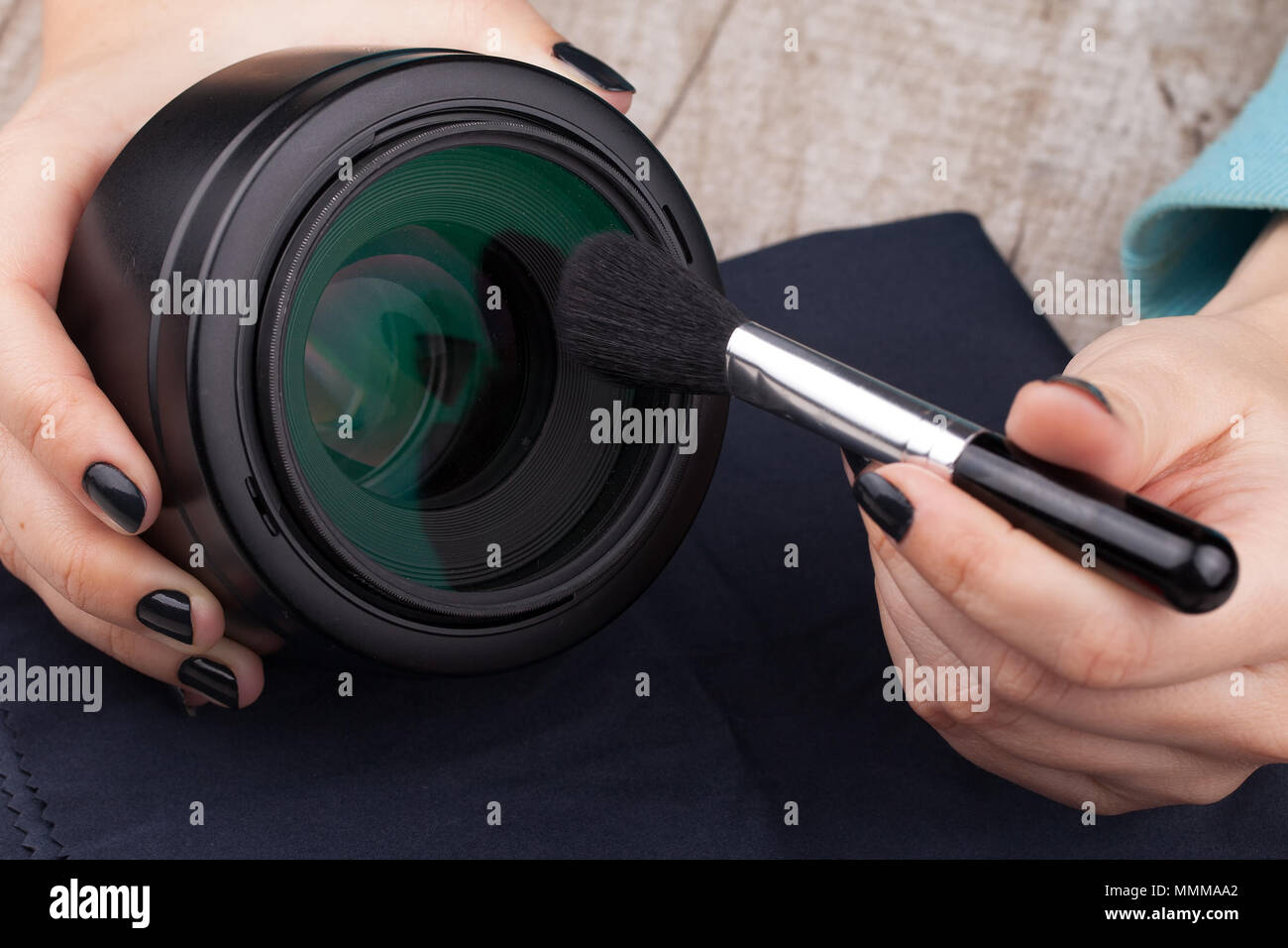 Il fotografo pulisce la lente di polvere su di un tavolo di legno. Close-up. Illuminazione da studio Foto Stock