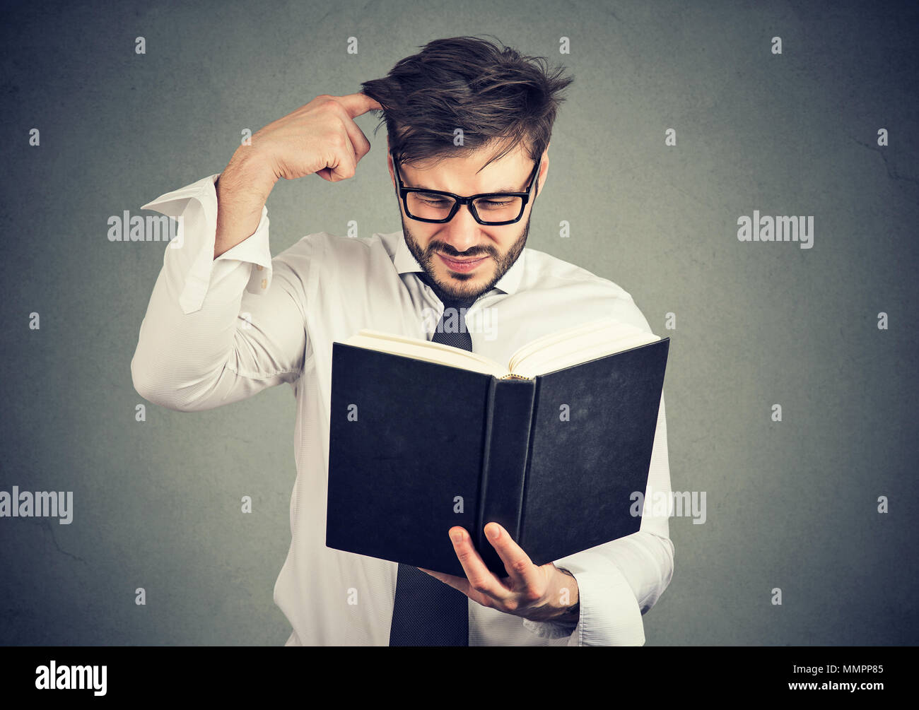 Giovane uomo confuso di graffiare la testa durante il tentativo di leggere il libro di smart malintesi contenuti. Foto Stock