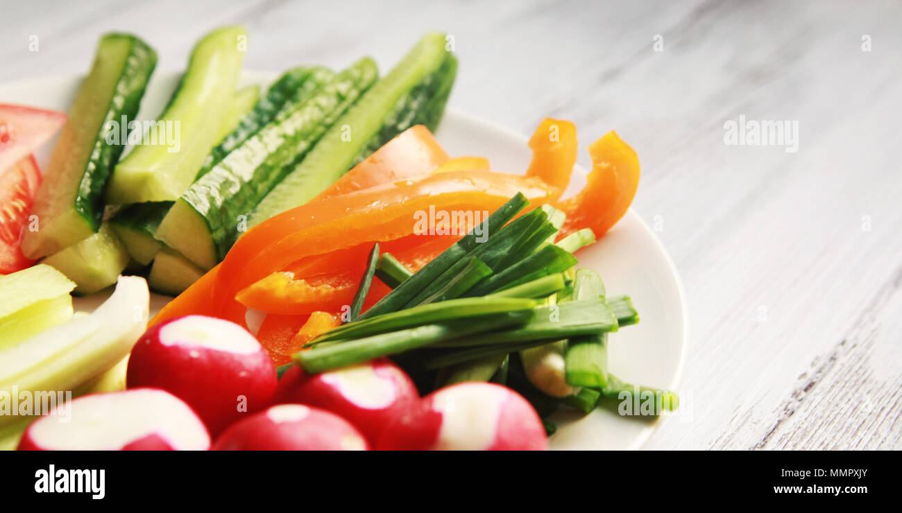 Piastra bianca con verdure per un vegetariano insalata. Ravanelli, pomodori, il sedano, il peperone verde, la cipolla e il cetriolo. Legno bianco tavolo da cucina. Close up. Foto Stock