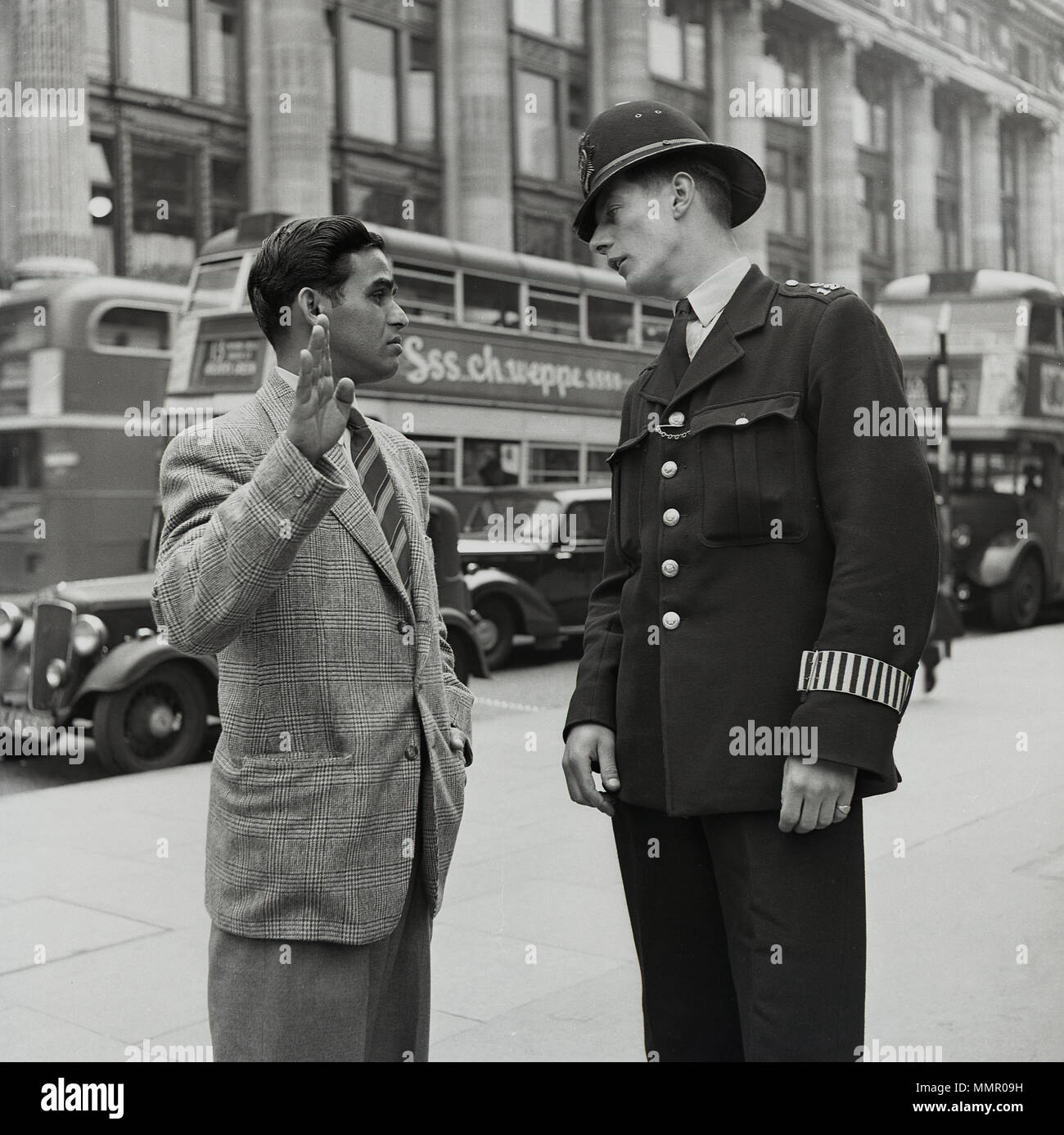 Degli anni Cinquanta, foto storiche, Oxford Street, Londra centrale, un neo arrivato ben vestito uomo dal Commonwealth chiede indicazioni da un poliziotto britannico. Foto Stock