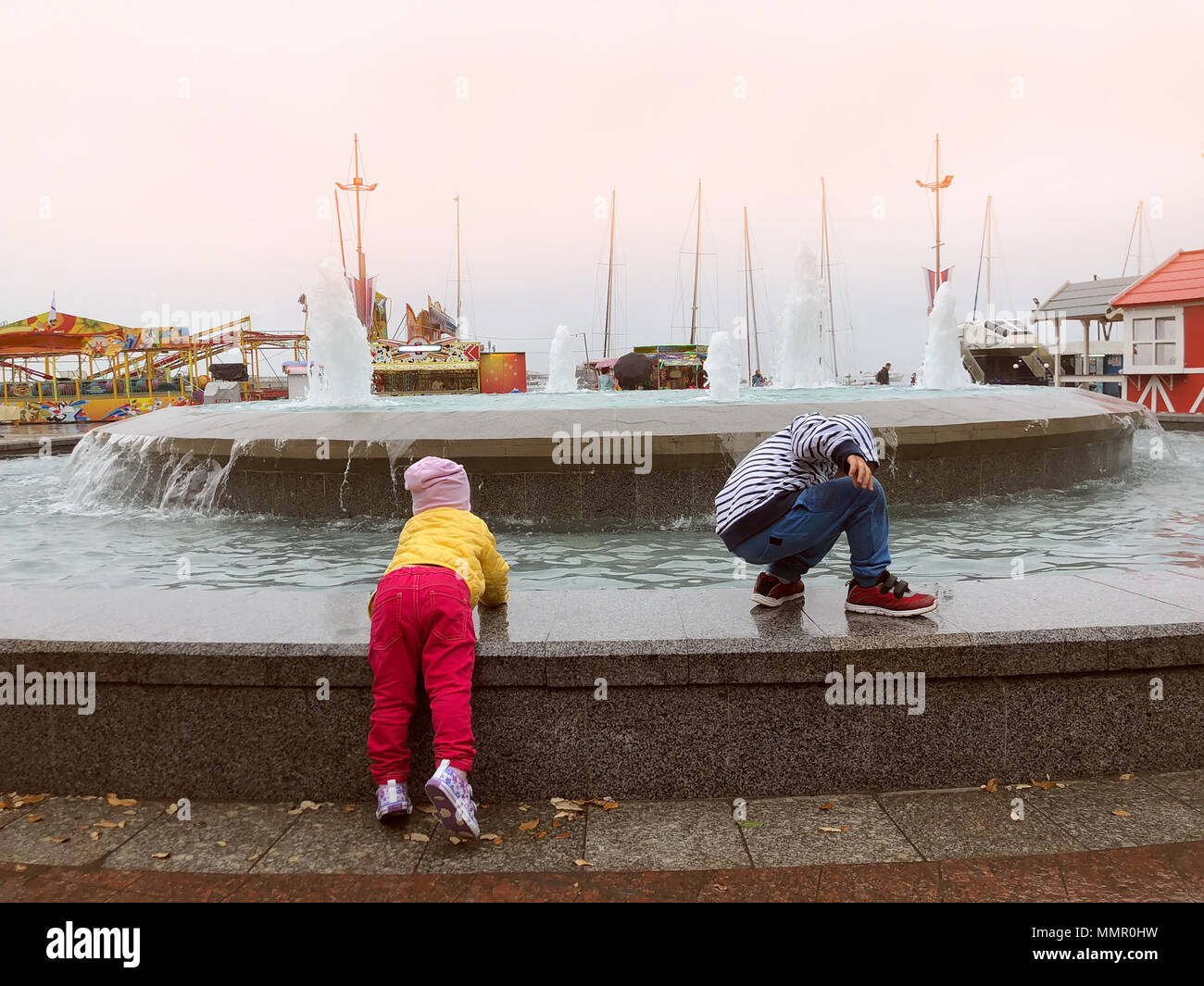 Due bambini giocare presso la Fontana torbida tempo piovoso. Lasciando i bambini senza cura per adulti. Gioco pericoloso. Foto Stock