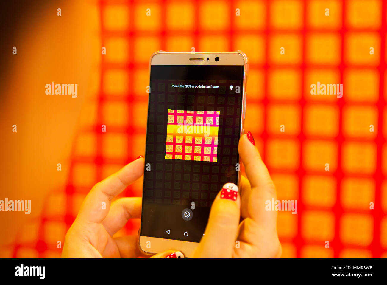 Una signora della mano che tiene un Huawei smart phone per eseguire la scansione del codice QR sulla parete Foto Stock