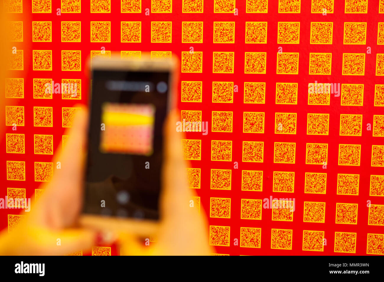 Una signora della mano che tiene un telefono intelligente per eseguire la scansione del codice QR sulla parete Foto Stock