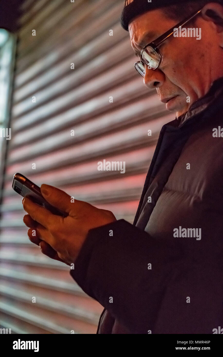 La città di New York New York, Feb 14, 2018: l'uomo guarda il suo smart phone davanti a un negozio griglia Foto Stock