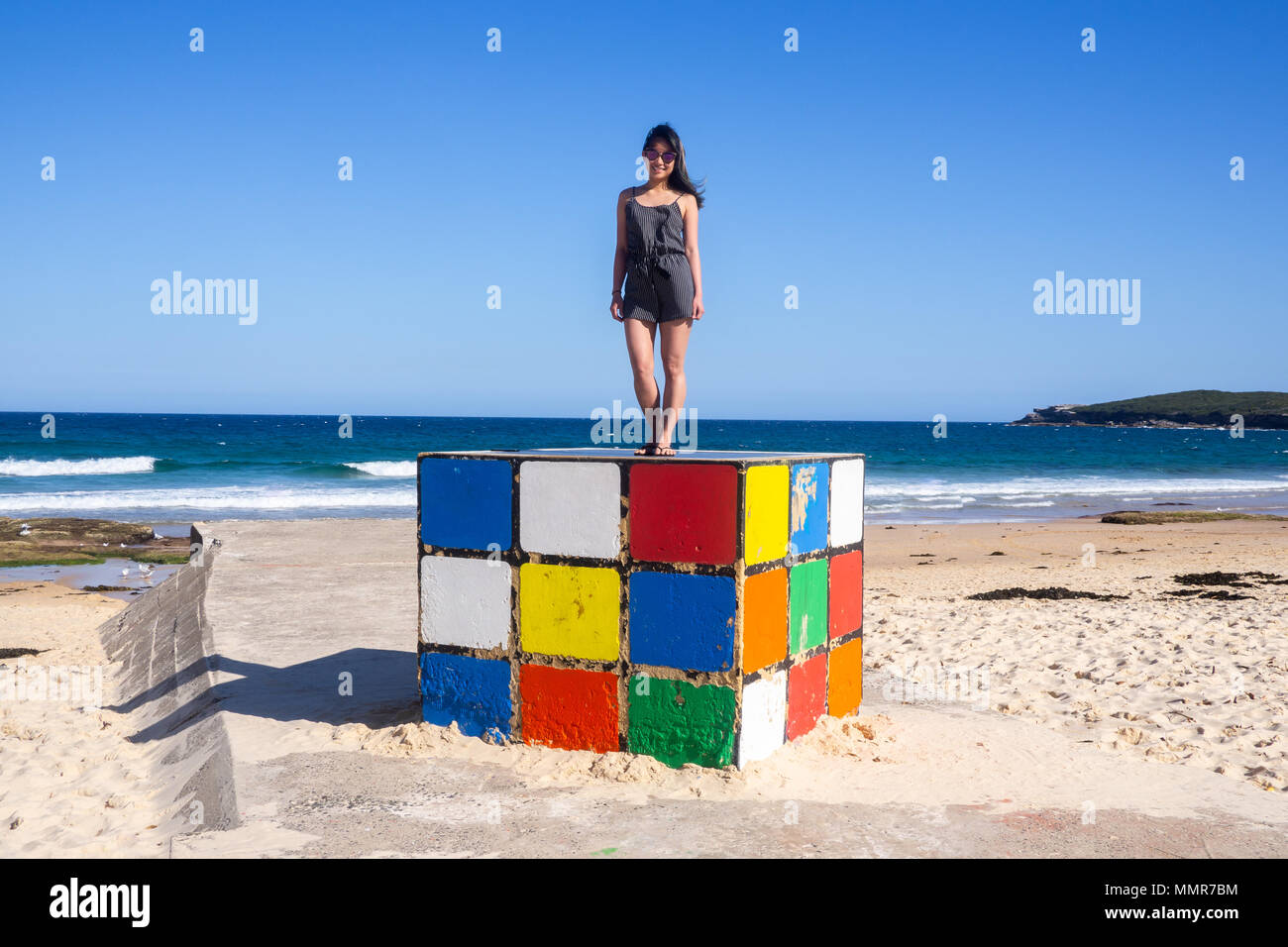 Giovane donna sorge su un gigantesco cubo di Rubik a Maroubra Beach, Sydney, Australia Foto Stock