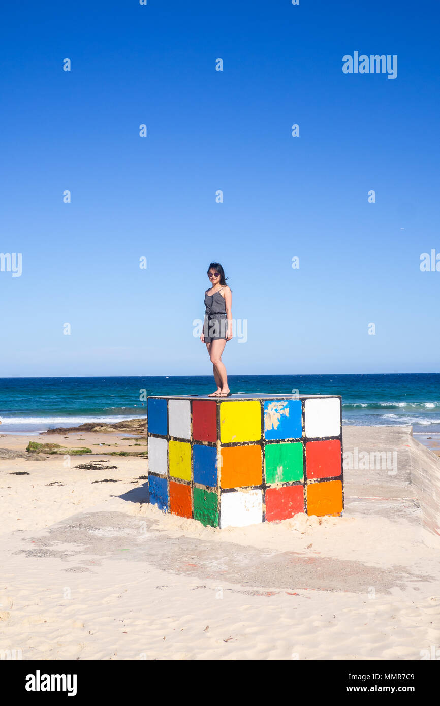 Giovane donna sorge su un gigantesco cubo di Rubik a Maroubra Beach, Sydney, Australia Foto Stock
