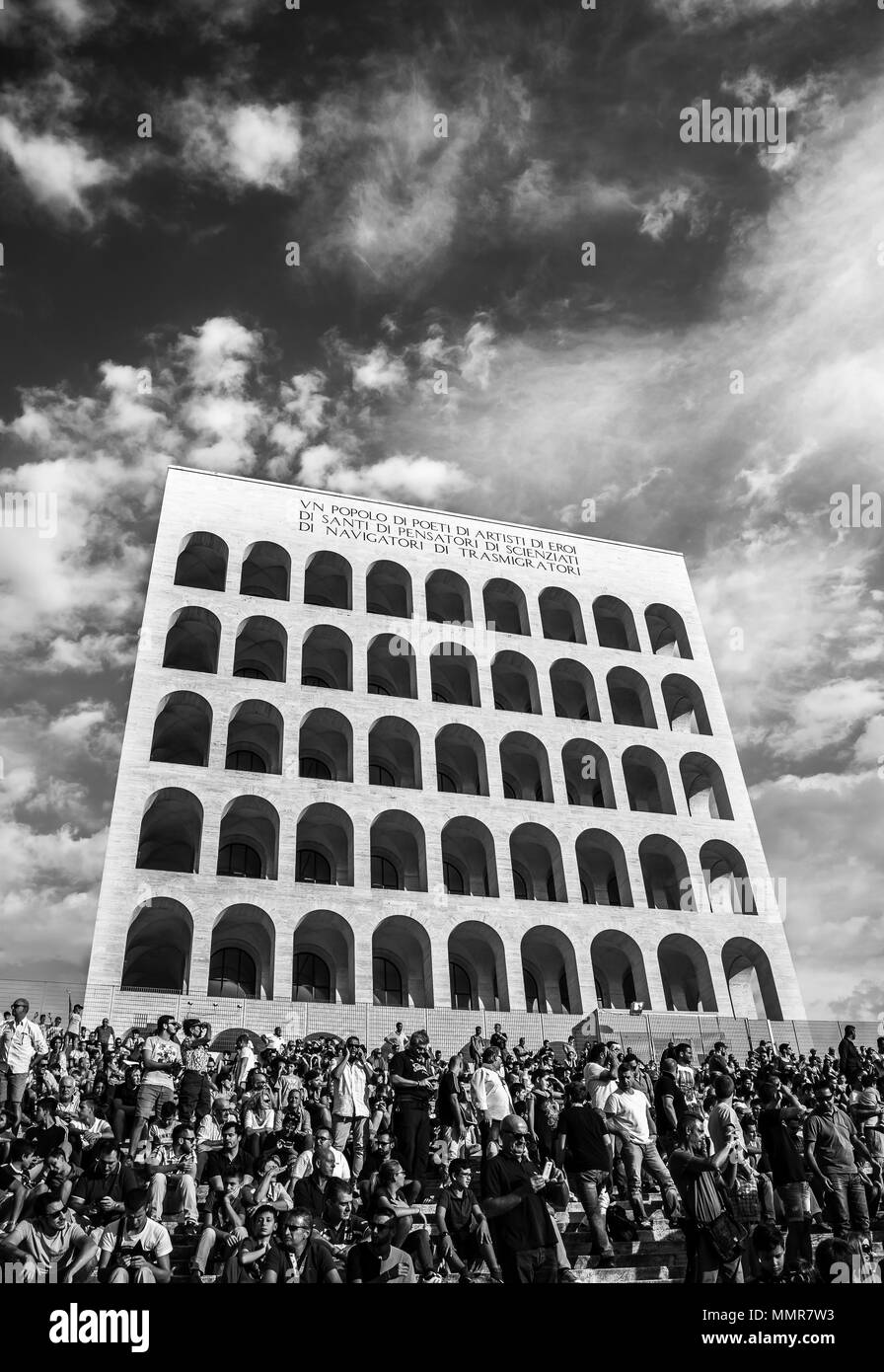 Il Palazzo della Civiltà Italiana, chiamato Colosseo quadrato, con molte persone sulle scale durante un evento sotto un cielo nuvoloso in bianco e nero Foto Stock