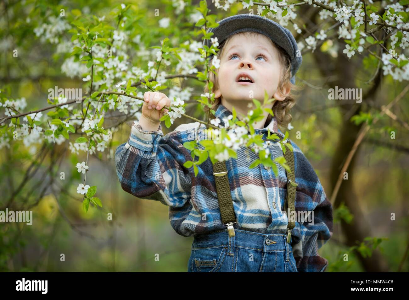 Giovane ragazzo biondo in posa di frutteti in fiore in primavera. Foto Stock