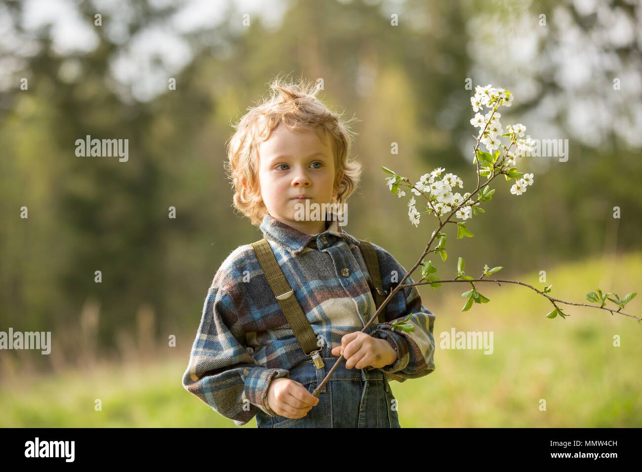 Giovane ragazzo biondo in posa di frutteti in fiore in primavera. Foto Stock