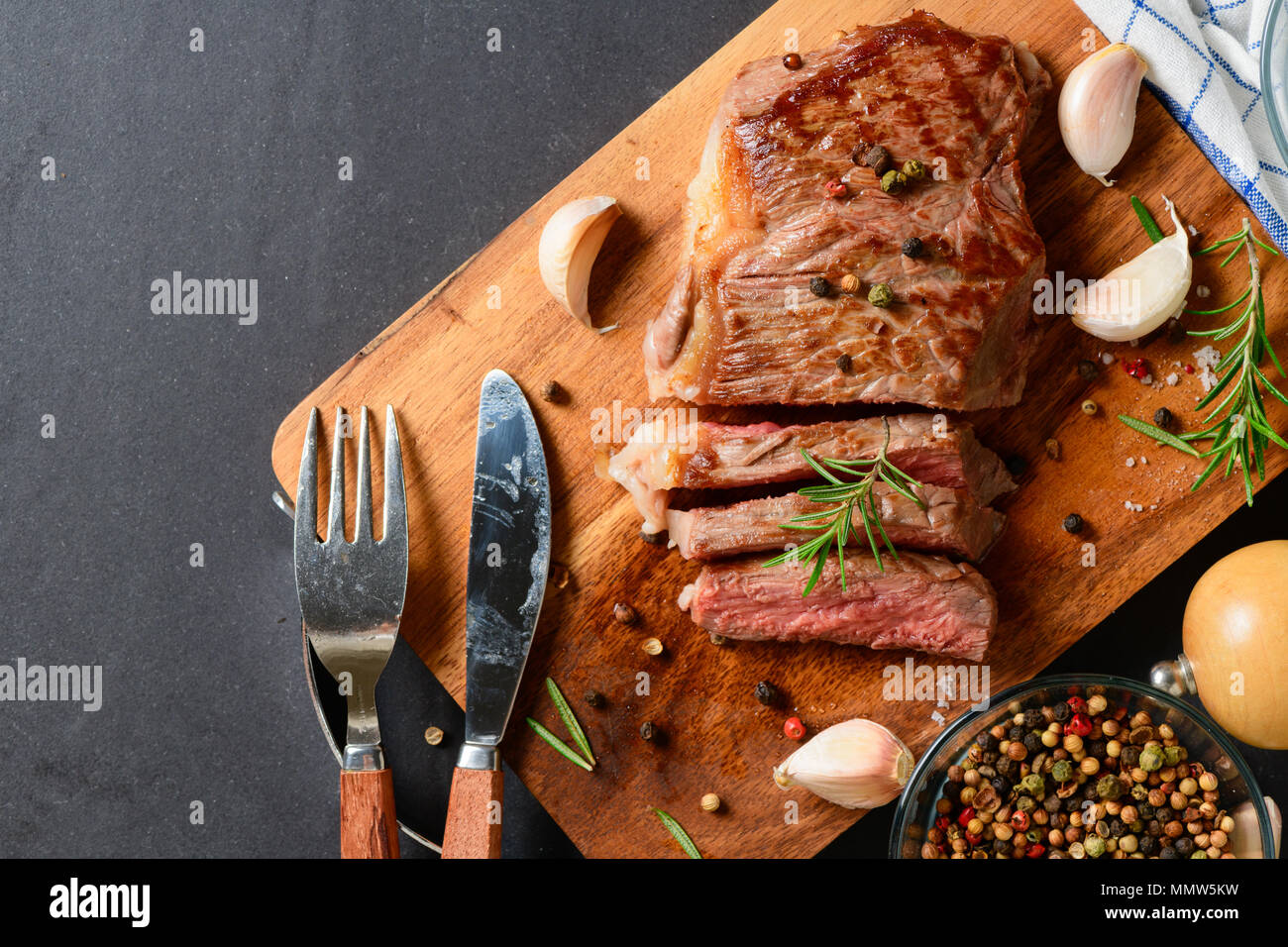 Tagliate a fette grigliate di carne di manzo con spezie, sale di aglio e rosmarino foglia sul balck tabella Foto Stock