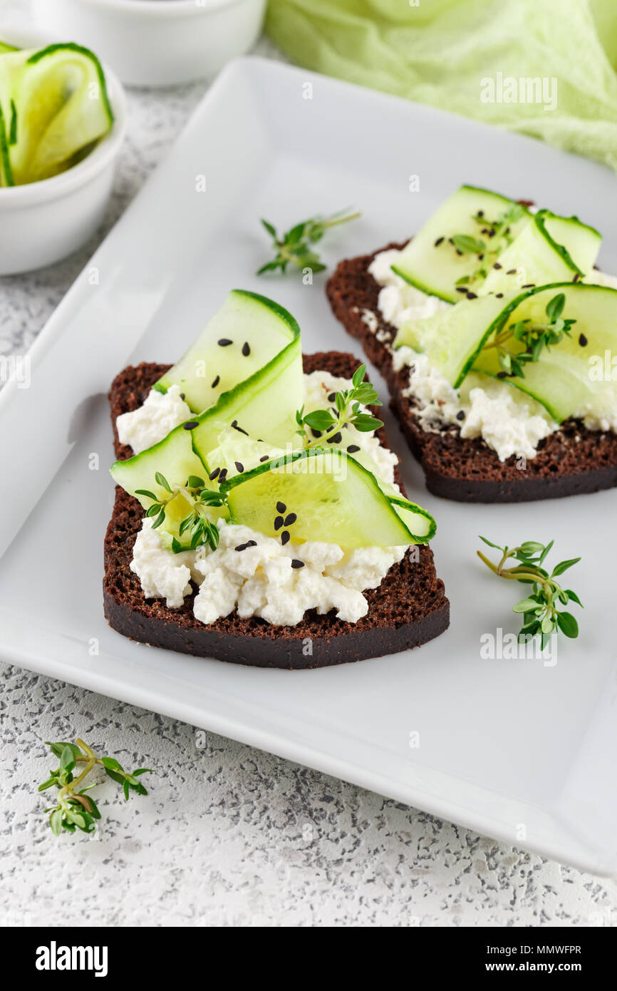 Crostini di pane di segale con ricotta, cetriolo e sesamo nero su grigio ardesia e pietra o calcestruzzo sfondo. Foto Stock