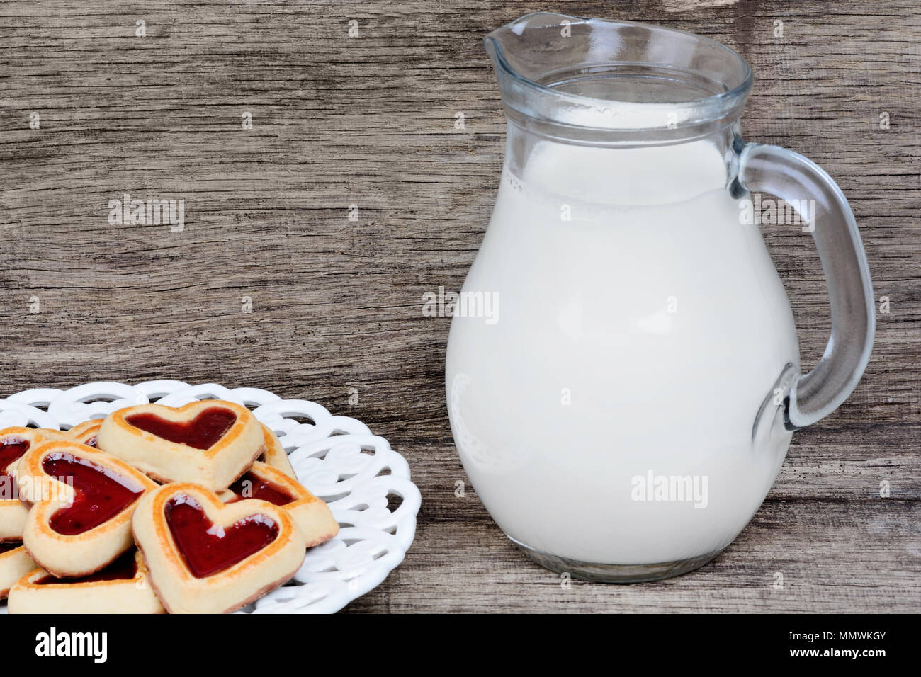 Cuore i cookie in una piastra con la brocca del latte sul tavolo di legno Foto Stock