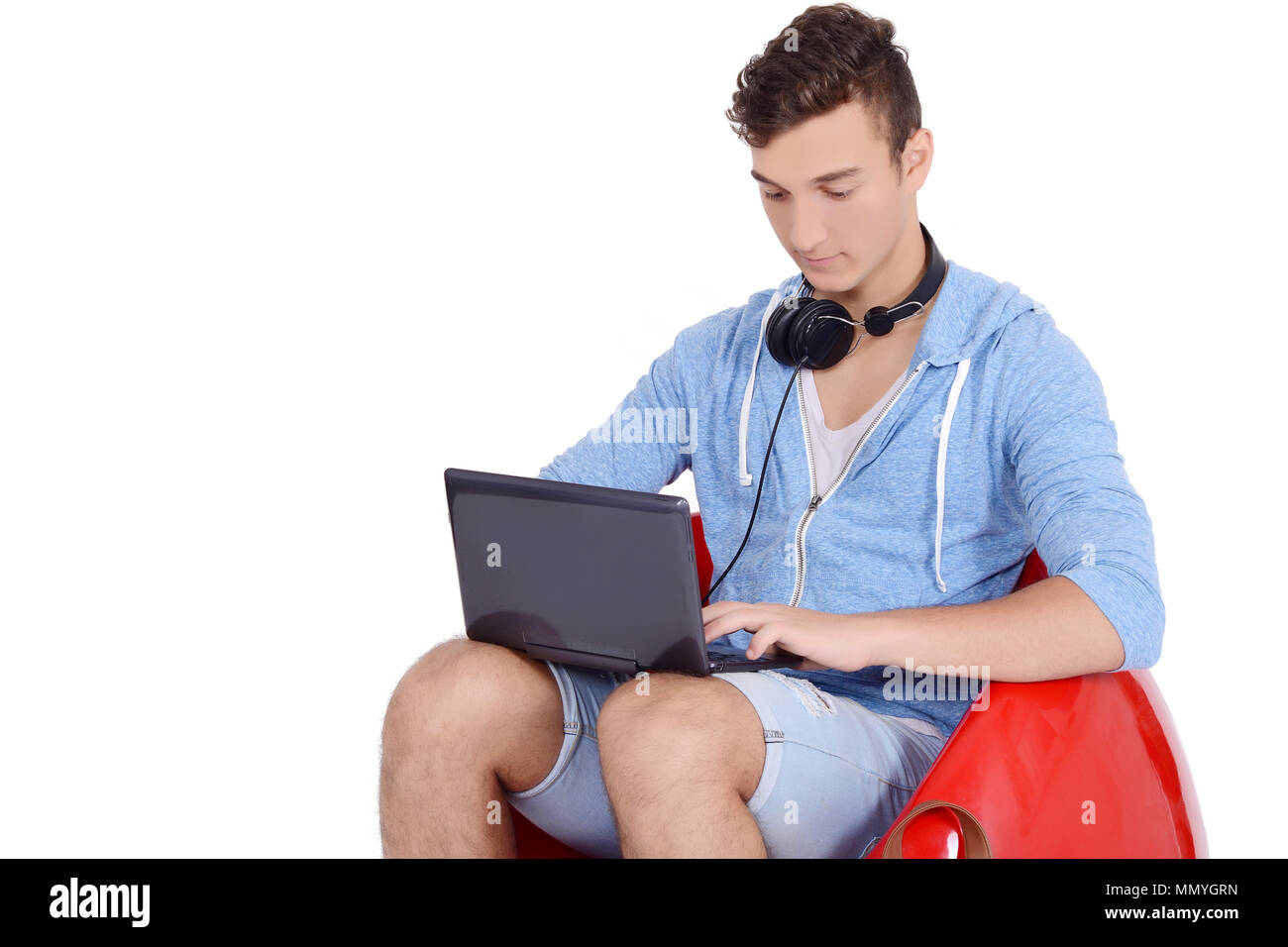 Chiusura del giovane uomo seduto in rosso pouf utilizzando laptop con lo zaino. Il concetto di istruzione Foto Stock