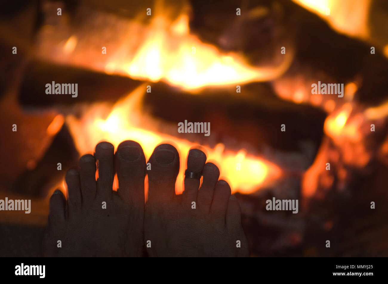 Diffrange la luce intorno a una silhouette delle dita dei piedi un riscaldamento di un incendio. Foto Stock
