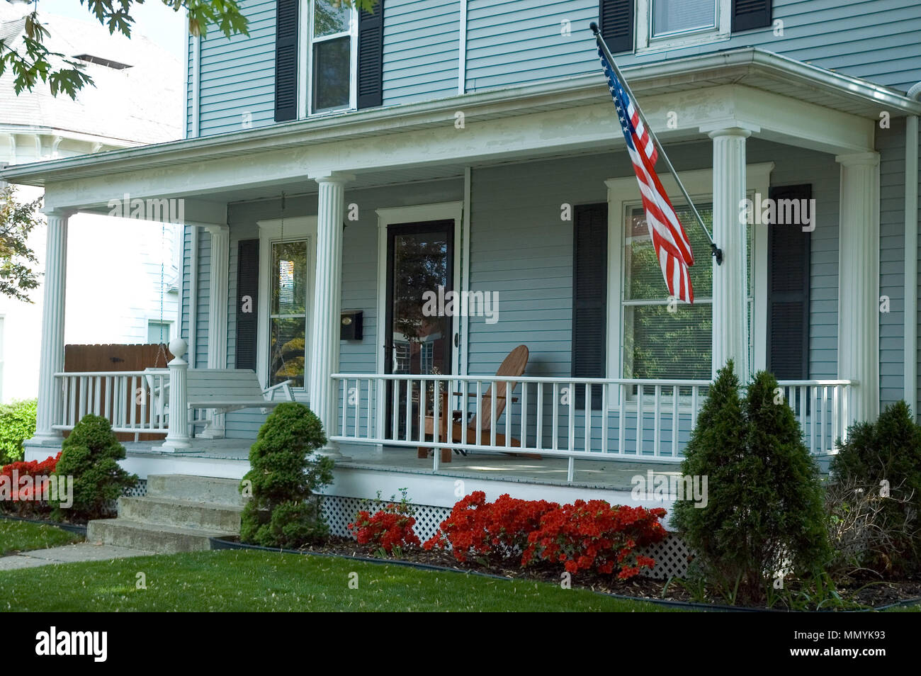 Un tipico portico anteriore di una casa in una piccola cittadina in U.S.A.  Dotato di una bandiera americana orgogliosamente battenti e un portico swing  di godersi la giornata di primavera Foto stock -