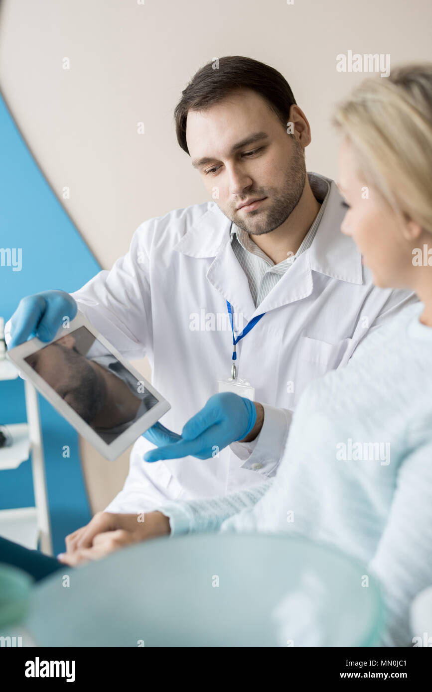 Uomo Barbuto in studio dentistico che mostra il tablet PC alla giovane cliente avente la consultazione in armadio. Foto Stock