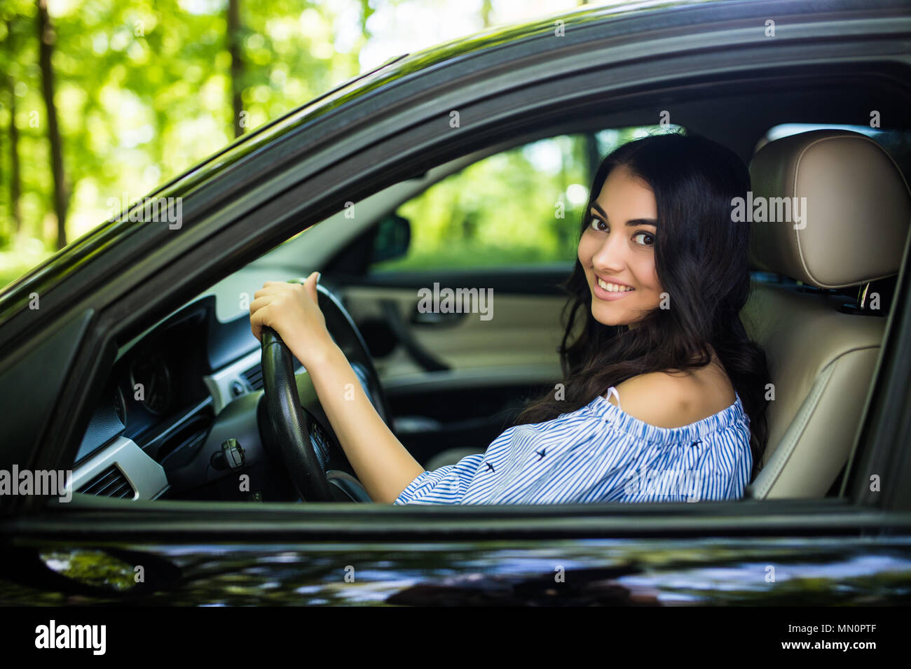 Giovane donna alla guida di una vettura in città. Ritratto di una donna bella in un auto, guardando fuori della finestra e sorridente. Foto Stock