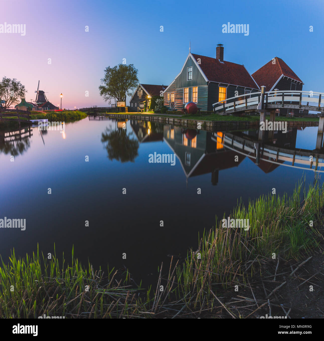 Case in legno e il mulino a vento sono riflesse nelle acque blu del fiume Zaan Zaanse Schans Olanda settentrionale dei Paesi Bassi in Europa Foto Stock