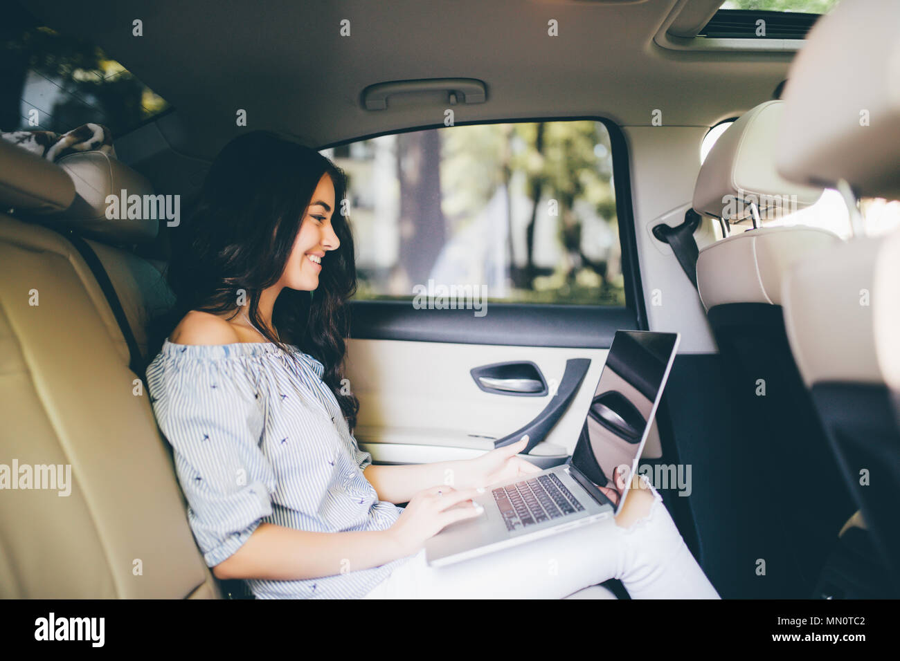 Bella donna d'affari sta usando un computer portatile mentre è seduto sul sedile posteriore in auto Foto Stock